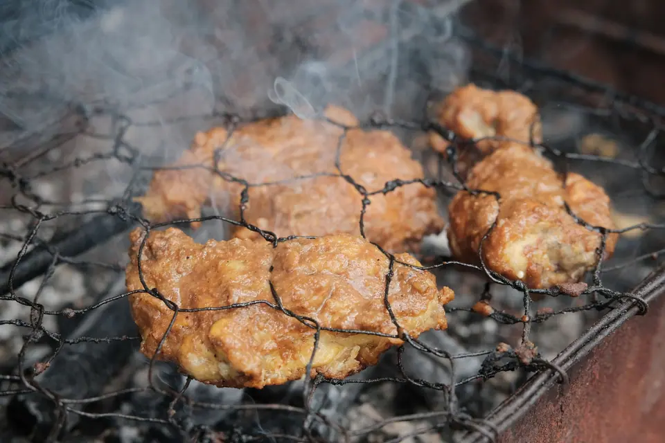 Potongan ayam berbumbu dibakar di atas bara arang dalam jepitan kawat