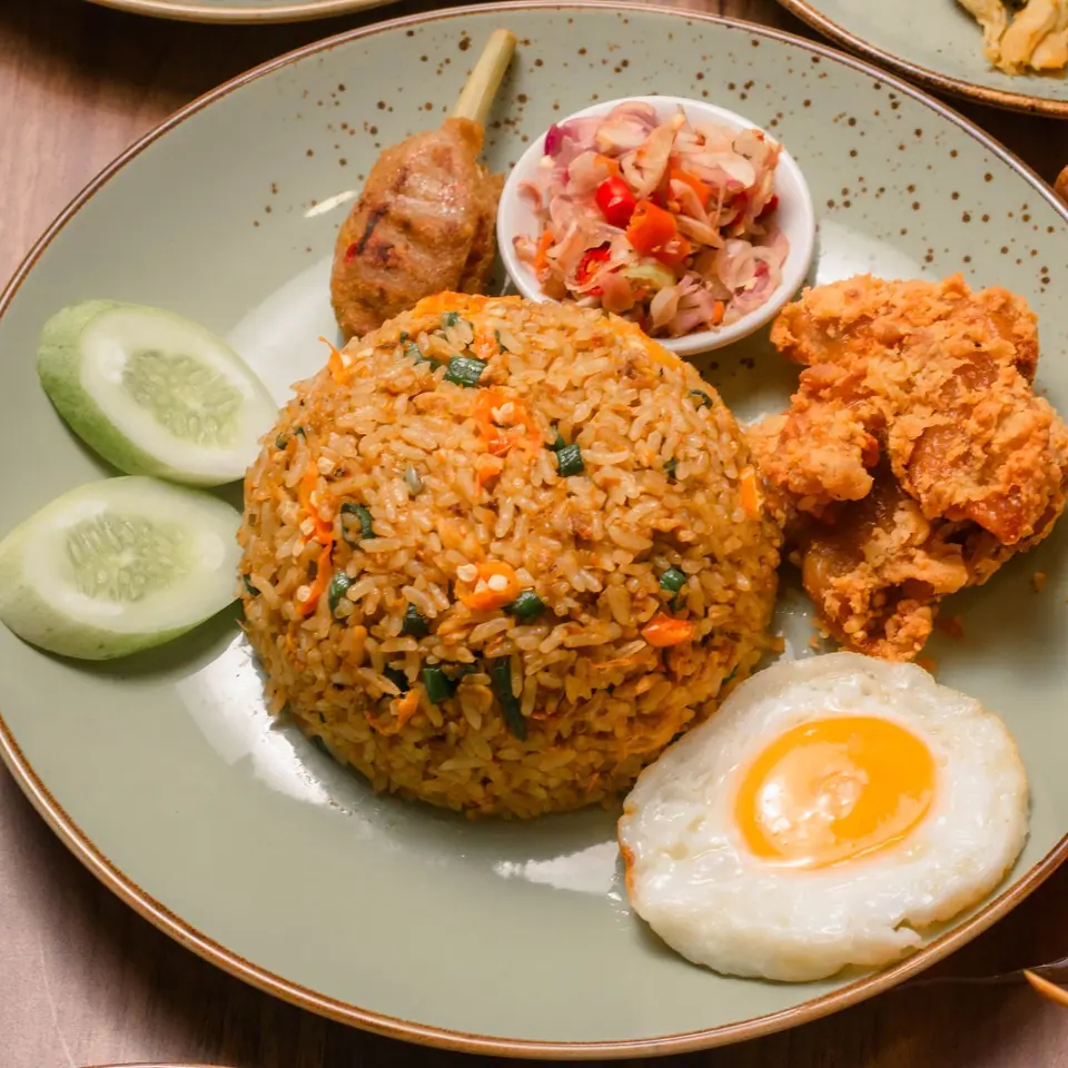 Nasi goreng dengan telur mata sapi, ayam goreng, dan irisan timun