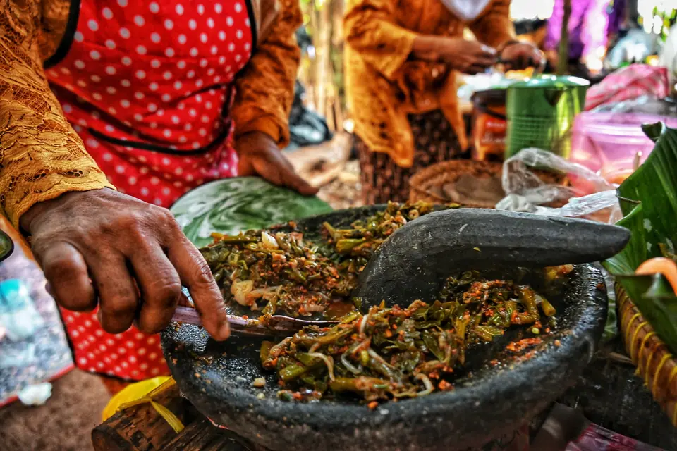 Tangan mengulek bumbu dan sayur di cobek batu